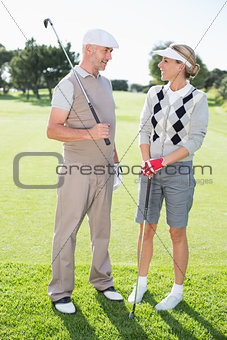 Golfing couple smiling at each other holding clubs