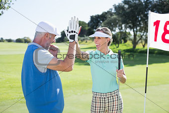 Golfing couple high fiving on the golf course at eighteenth hole