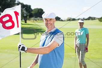 Happy golfer holding eighteenth hole flag with partner behind him