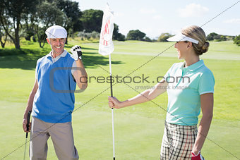 Lady golfer holding eighteenth hole flag for cheering partner