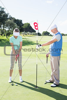 Golfer holding eighteenth hole flag for partner putting ball