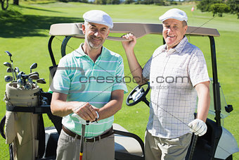 Golfing friends standing beside their buggy smiling at camera