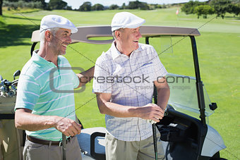 Golfing friends standing beside their buggy smiling