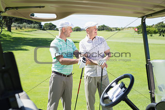 Golfing friends standing beside their buggy looking around