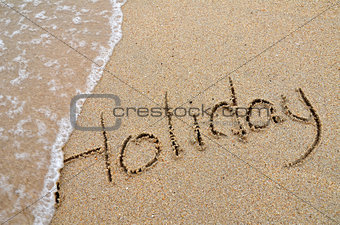 Holiday word written on sandy beach