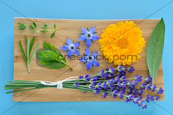 Summer herbs and edible flowers on wooden plate.