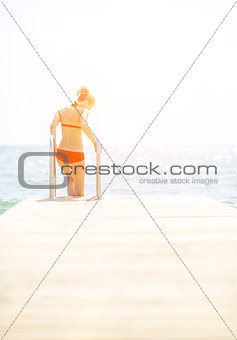 Young woman going down into sea from bridge. rear view