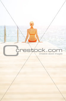Young woman sitting on bridge. rear view