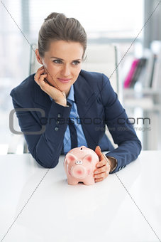 Portrait of thoughtful business woman with piggy bank
