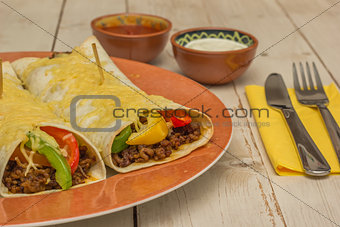 Burritos filled with ground beef and peppers, topped with cheese