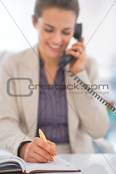 Closeup on business woman talking phone and writing in diary