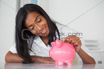 Smiling businesswoman putting coins into piggy bank at her desk