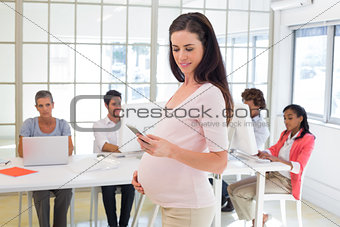 Pregnant office worker touches bump and texts on phone