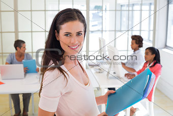 Pregnant businesswomen with folders with colleagues behind