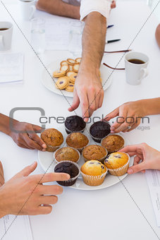 Business people taking muffins from plate