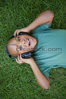 Little boy lying on grass listening to music smiling at camera