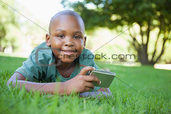 Little boy lying on grass holding digital camera smiling at camera