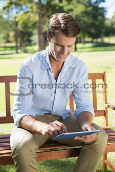 Smiling man sitting on park bench using tablet
