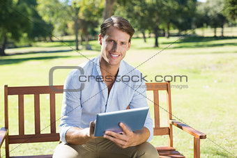 Smiling man sitting on park bench using tablet looking at camera