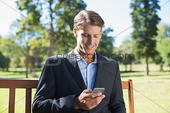 Casual businessman texting on phone on park bench