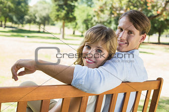 Couple relaxing on park bench together smiling at camera