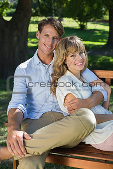 Affectionate couple relaxing on park bench together smiling at camera