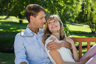 Affectionate couple relaxing on park bench together smiling at each other
