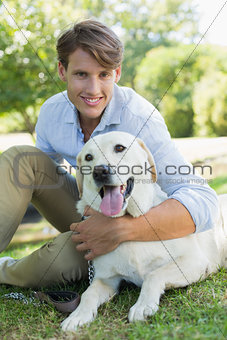 Handsome smiling man with his labrador sitting in the park