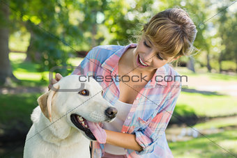 Pretty smiling blonde posing with her labrador in the park