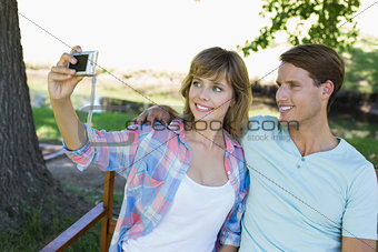 Cute couple sitting on bench in the park taking a selfie