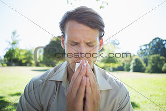 Stylish man blowing his nose in the park