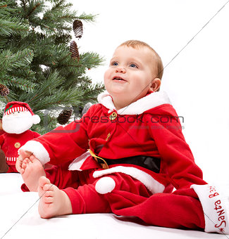 Santa Baby boy sitting next to Christmas tree.