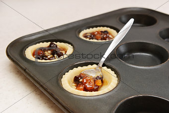 Spooning mincemeat into pastry cases 