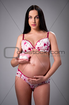 Lovely pregnant woman holding a pair of pink baby booties