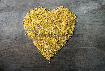 millet grains formed in heart shape on wooden background 