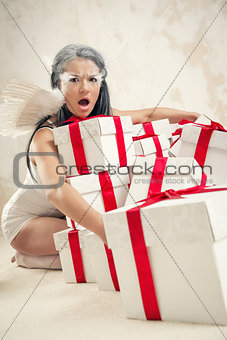 Beautiful young woman as angel with heap of gift boxes indoors