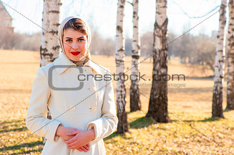 portrait of a girl in a white coat on the background of birch tr