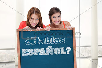 Composite image of teenage girls smiling while holding a blank poster and hiding behind it