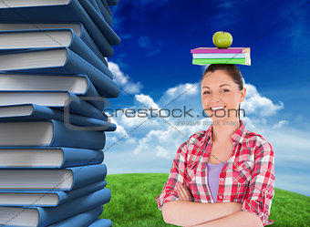 Composite image of pretty student holding an apple and books on her head