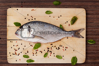 Fish on wooden board with herbs and spices.