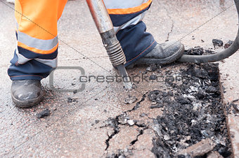 Road worker breaking street asphalt with jackhammer