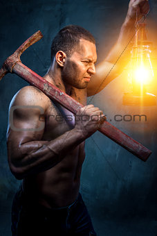 Muscular man holding pickaxe and oil lamp
