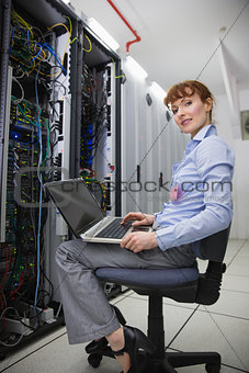 Happy technician sitting on swivel chair using laptop to diagnose servers
