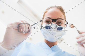 Dentist in surgical mask and dental loupes looking down over patient