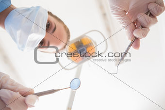 Dentist in surgical mask holding dental tools over patient