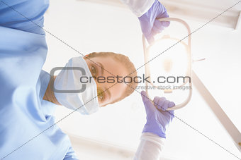 Dentist in surgical mask shining light over patient
