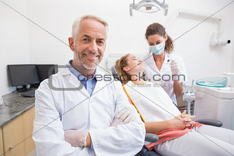 Dentist smiling at camera with assistant and patient behind