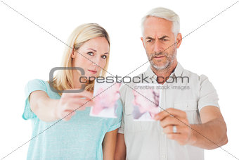 Unhappy couple holding two halves of torn photograph