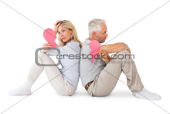 Unhappy couple sitting holding two halves of broken heart