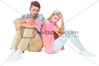 Attractive young couple sitting holding two halves of broken heart